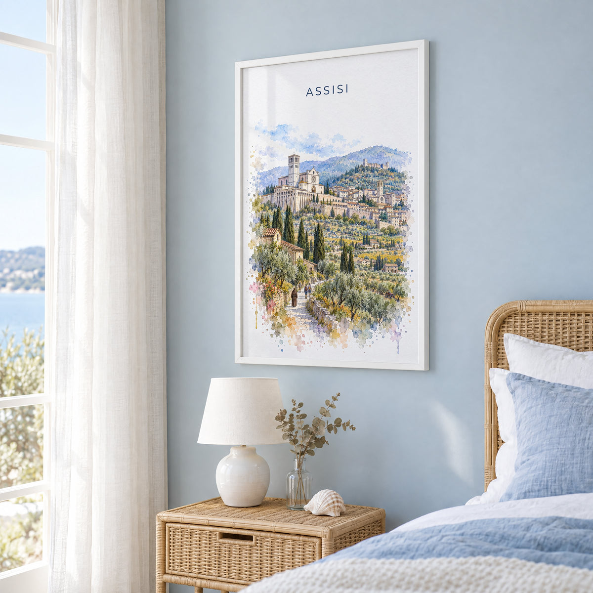 Assisi watercolor print in a white frame on a pale blue wall beside a rattan bed in a coastal bedroom
