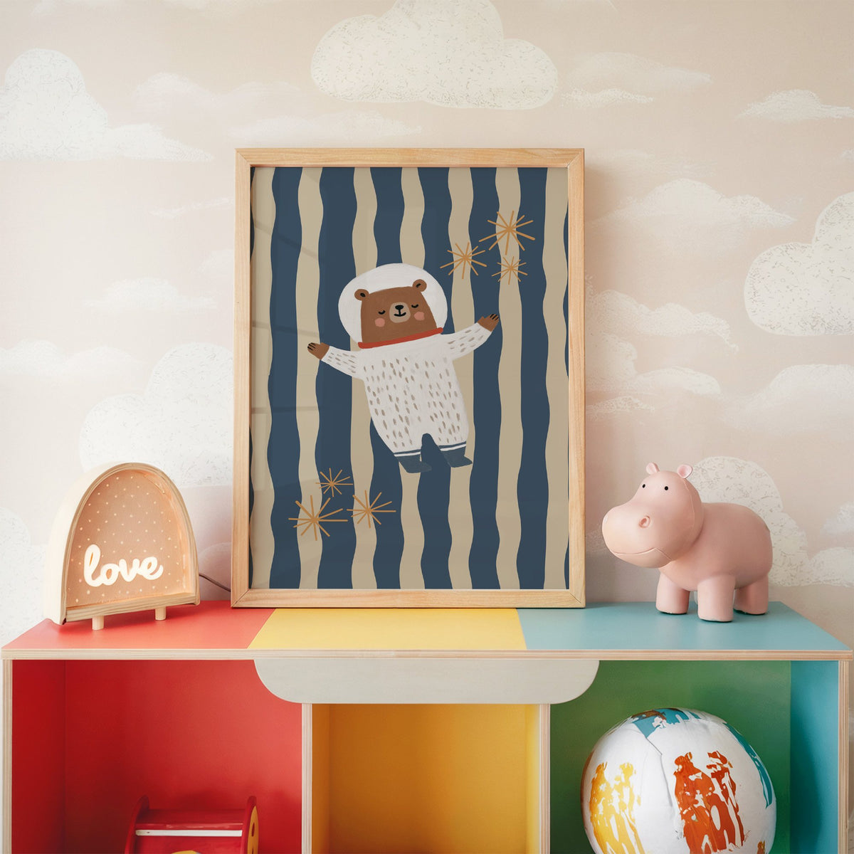 Astronaut bear wavy stripe nursery print in an oak frame on a rainbow toy shelf against cloud wallpaper