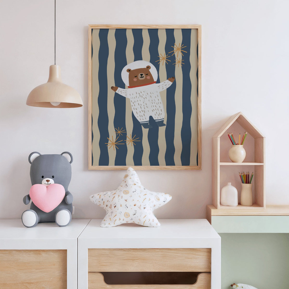 Astronaut bear wavy stripe nursery print in an oak frame above a white dresser with a star pillow and house shelf