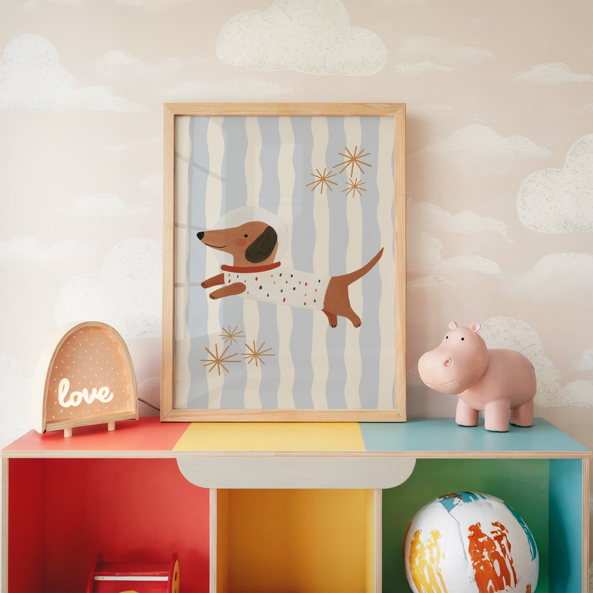 Astronaut dachshund wavy stripe nursery print in an oak frame on a rainbow toy shelf against cloud wallpaper