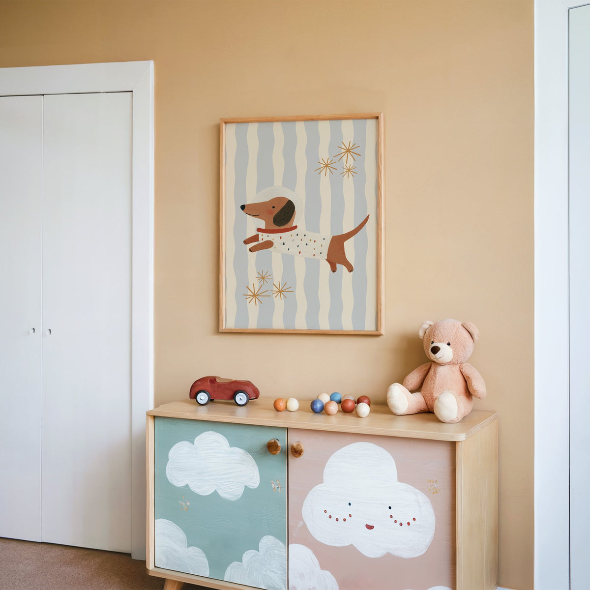 Astronaut dachshund wavy stripe nursery print in an oak frame on a peach wall above a cloud-painted cabinet