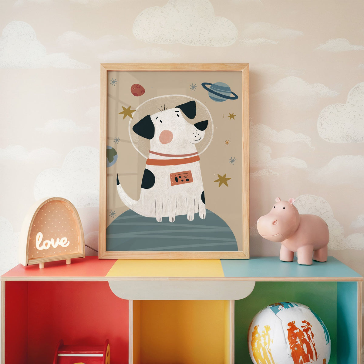 Spotted dog astronaut planet nursery print in an oak frame on a rainbow toy shelf against cloud wallpaper