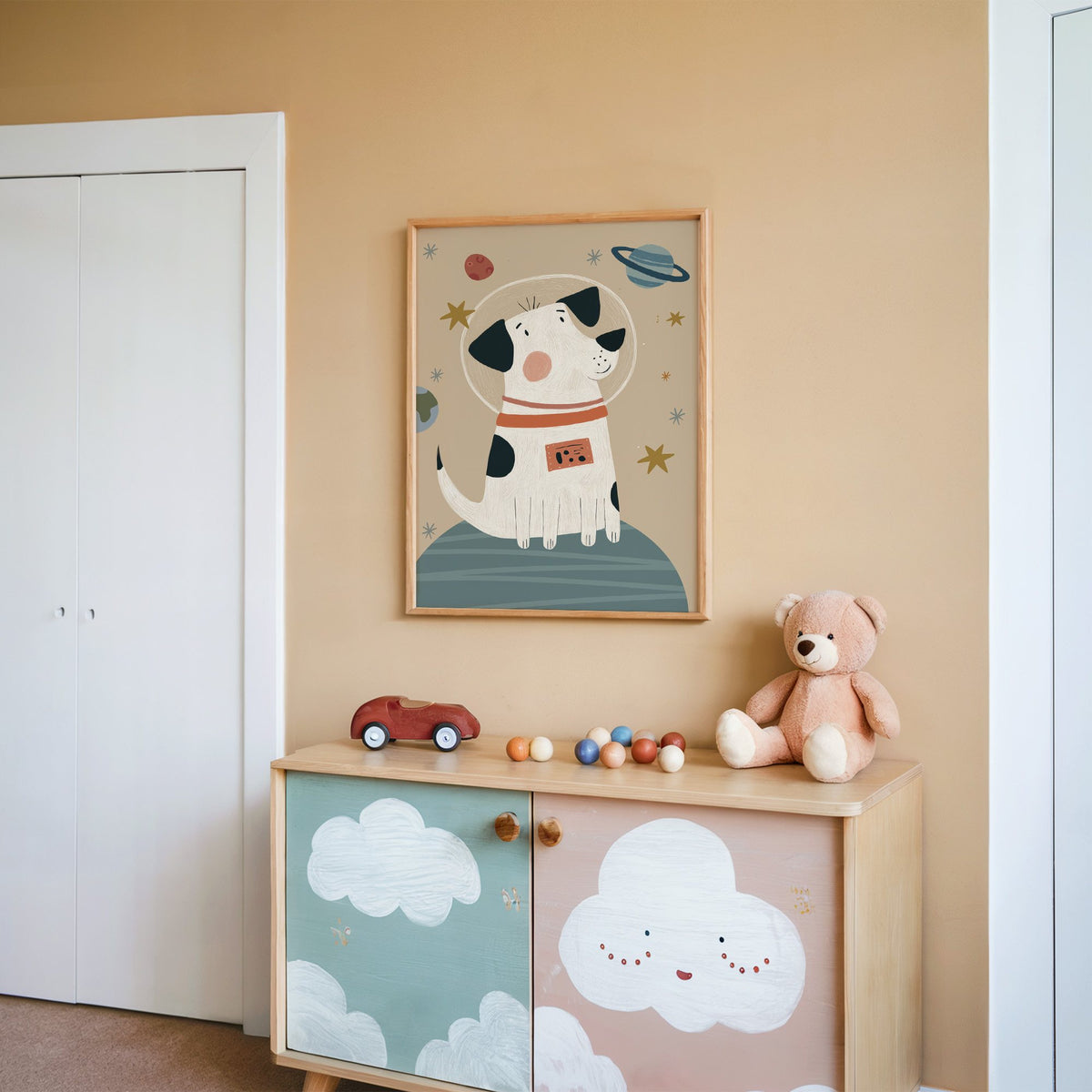 Spotted dog astronaut planet nursery print in an oak frame on a peach wall above a cloud-painted cabinet