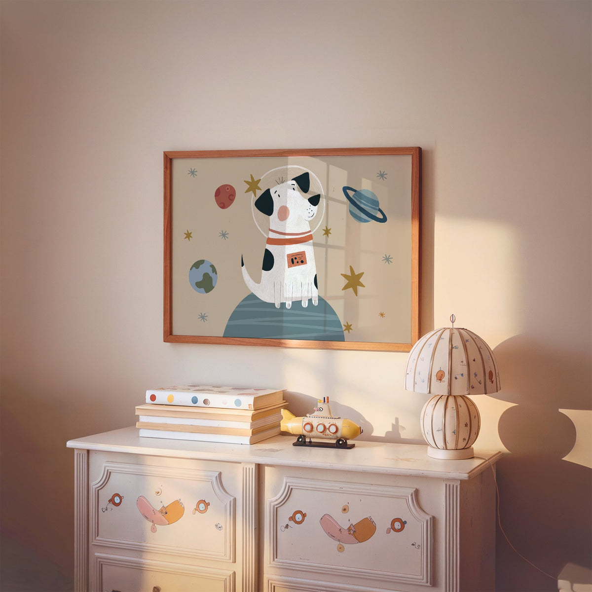 Landscape spotted dog astronaut planet nursery print in a cherry wood frame above a painted dresser and lamp