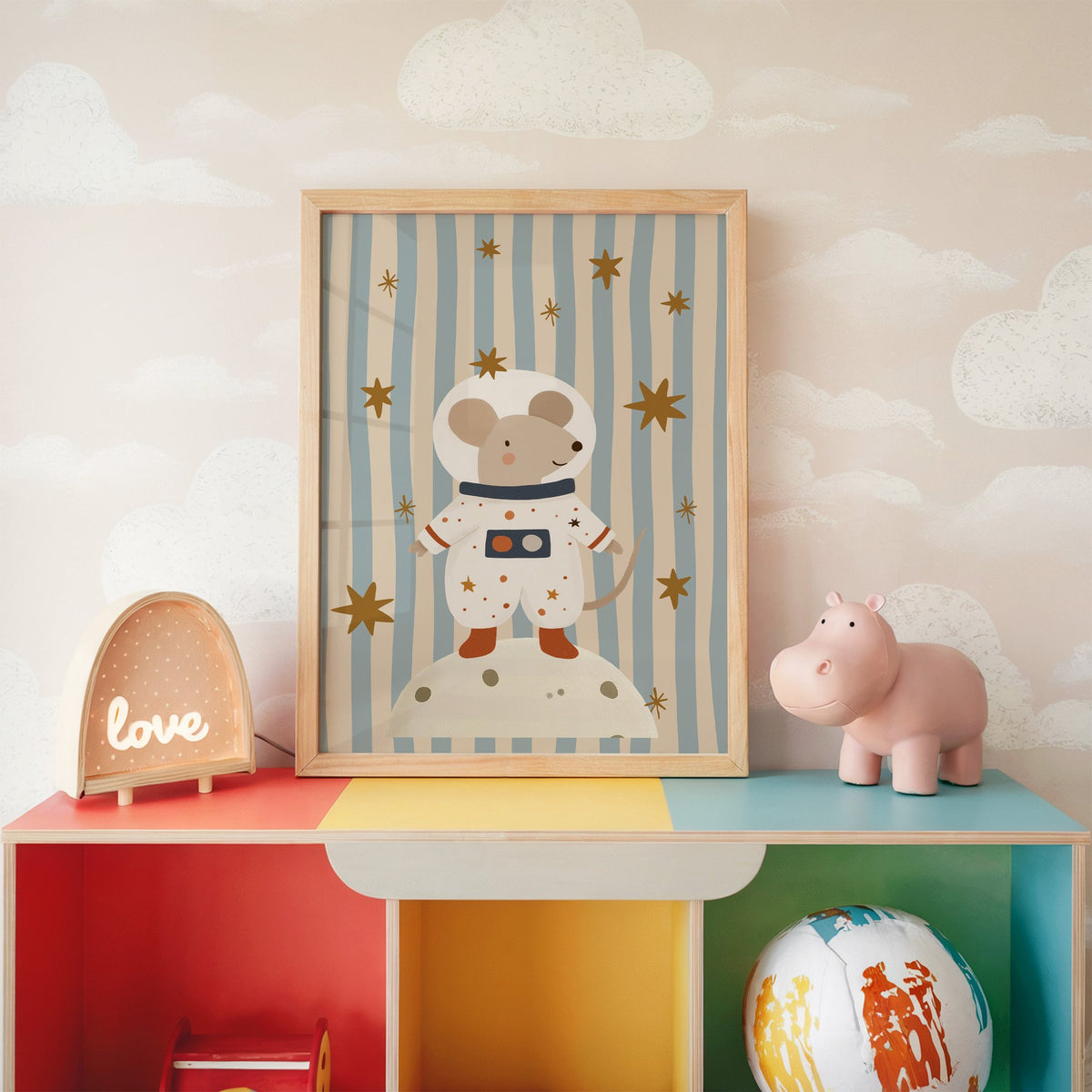 Astronaut mouse on the moon nursery print in an oak frame on a rainbow toy shelf against cloud wallpaper