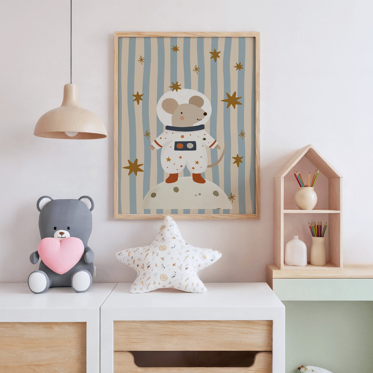 Astronaut mouse on the moon nursery print in an oak frame above a white dresser with a star pillow and house shelf