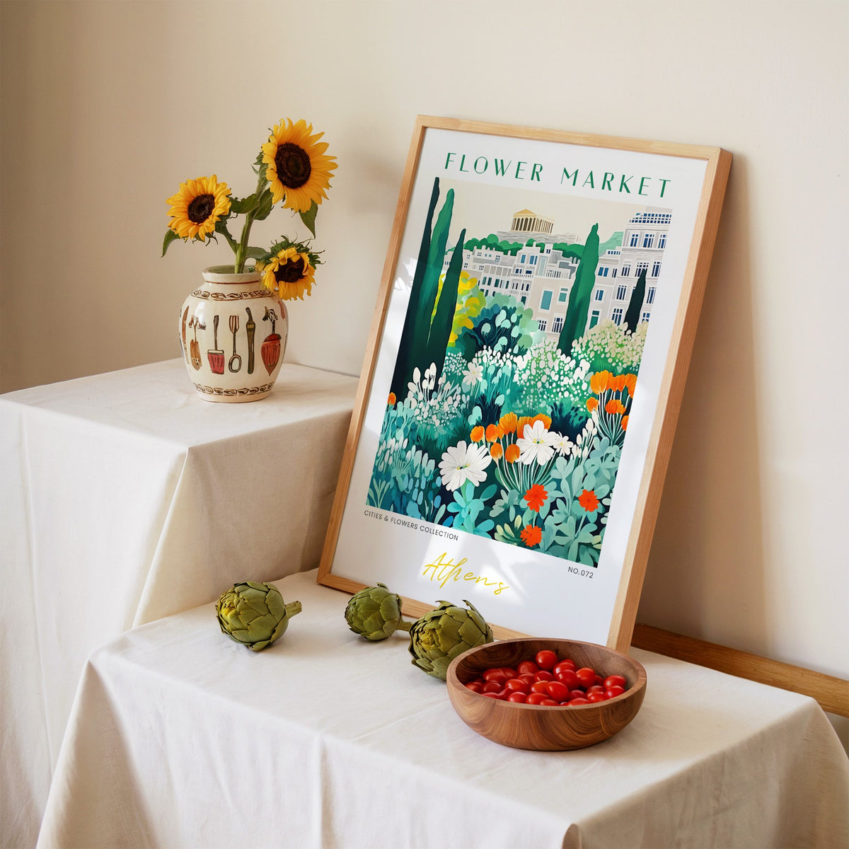 Athens flower market print in an oak frame leaning on a linen-draped table beside a vase of sunflowers
