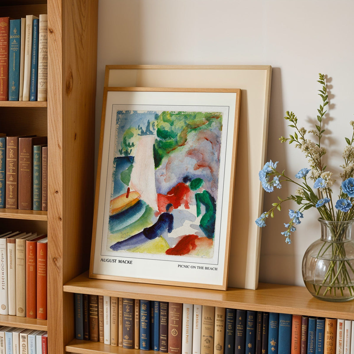 Beach watercolour in an oak frame leaning on a bookshelf beside blue flowers