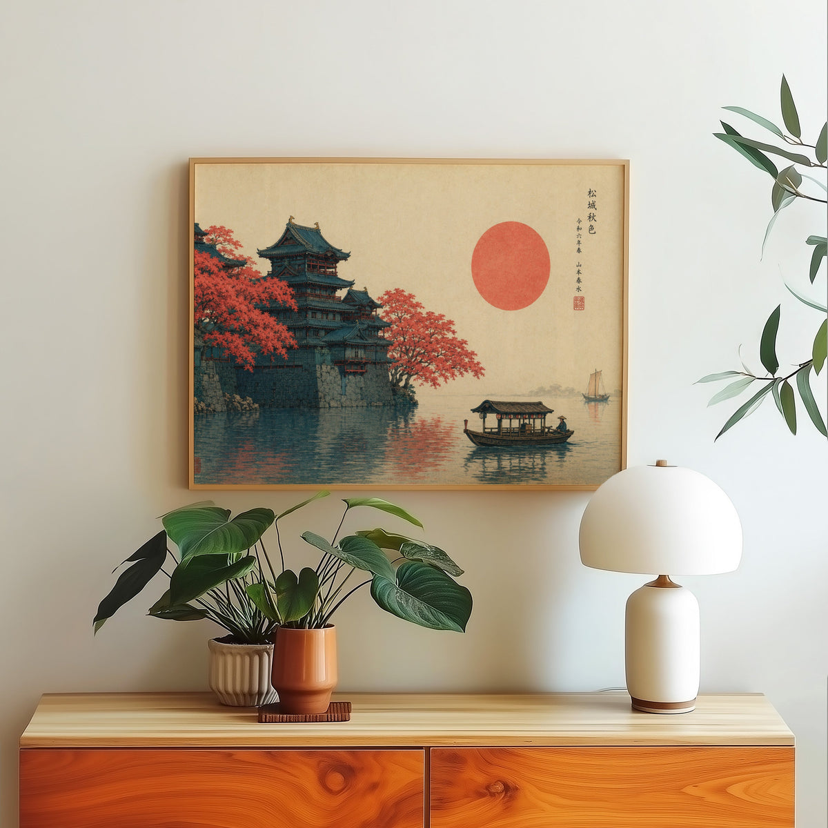 Autumn castle on a lake with red sun print in a light oak frame above a wood sideboard with a white dome lamp