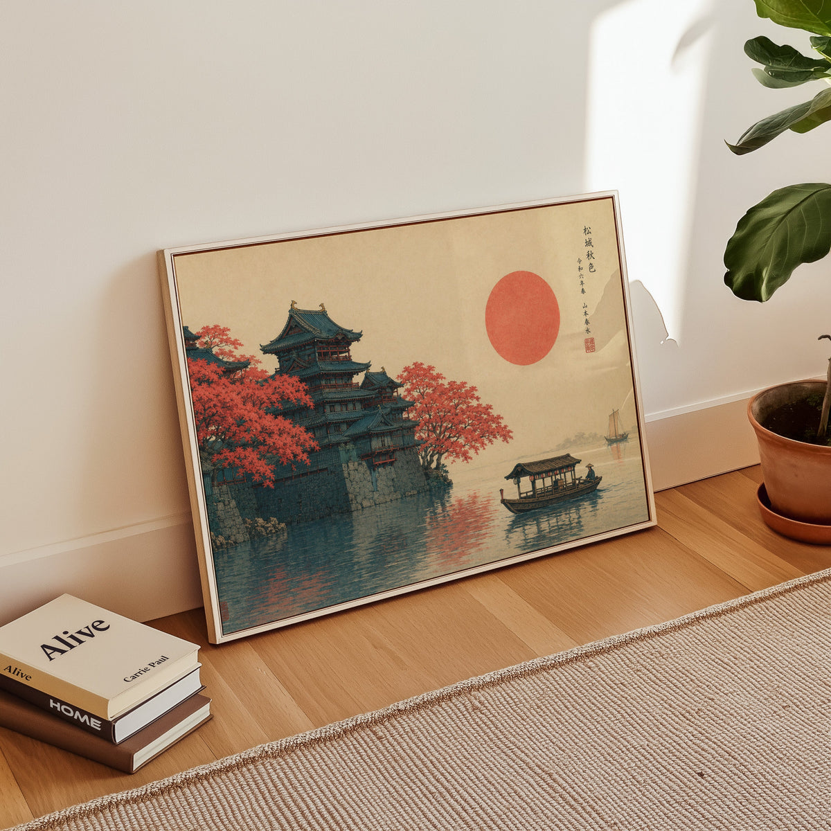 Autumn castle on a lake with red sun print in a white floater frame leaning on a wood floor beside stacked books