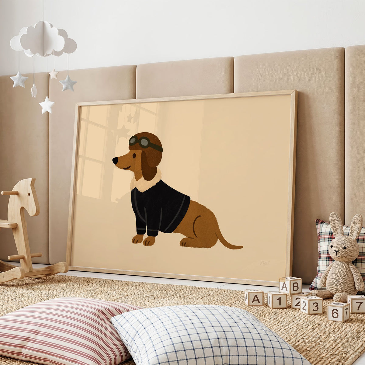 Dachshund in aviator cap nursery print in an oak frame on a padded wall by a wooden rocking horse