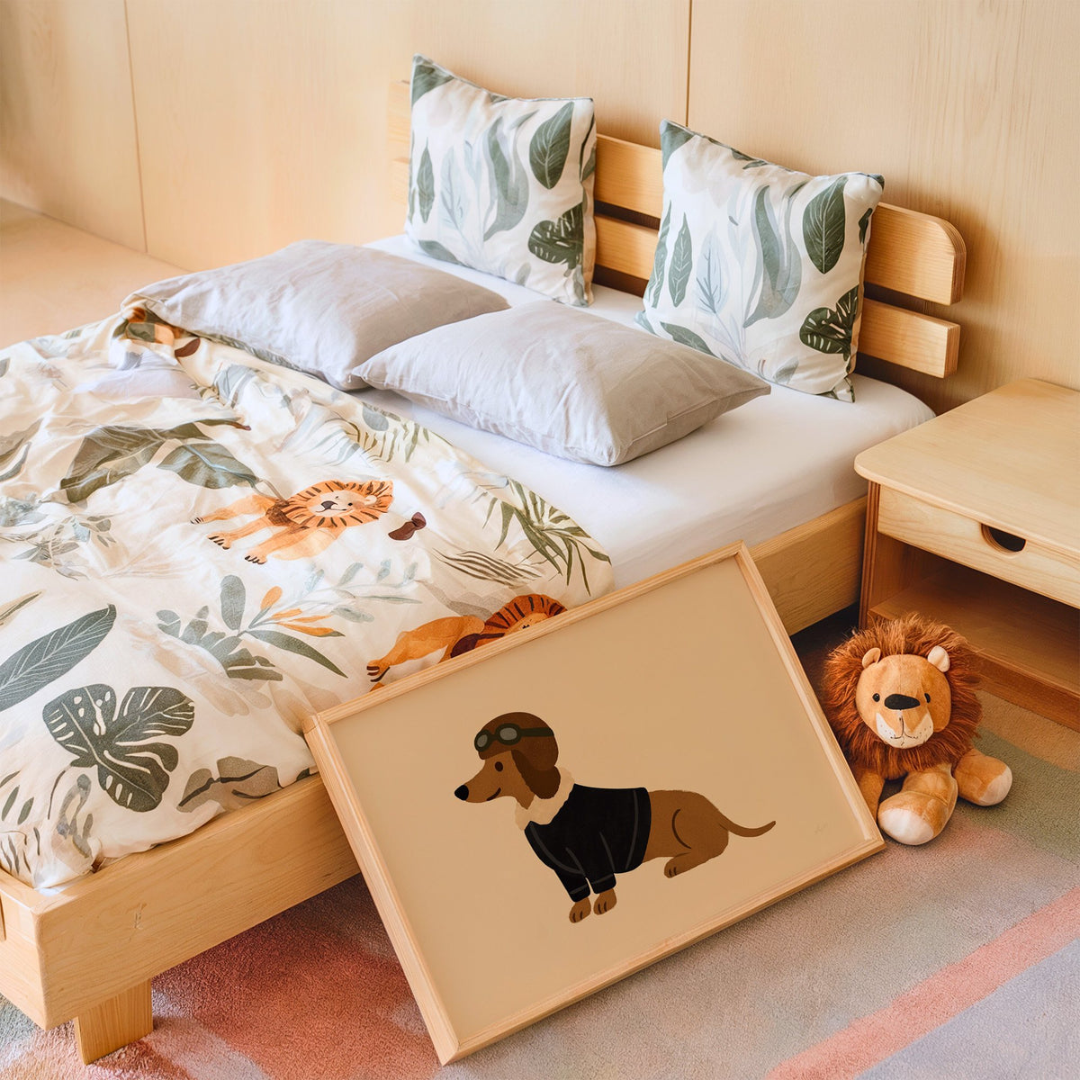 Dachshund in aviator cap nursery print in an oak frame leaning on a kids bed by a lion plush