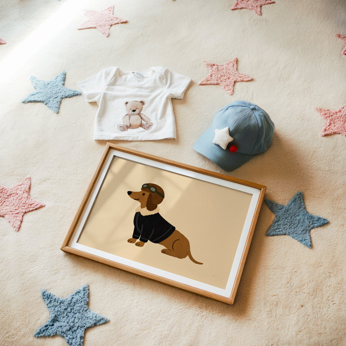 Dachshund in aviator cap nursery print in a matted oak frame on a star rug with a baby tee