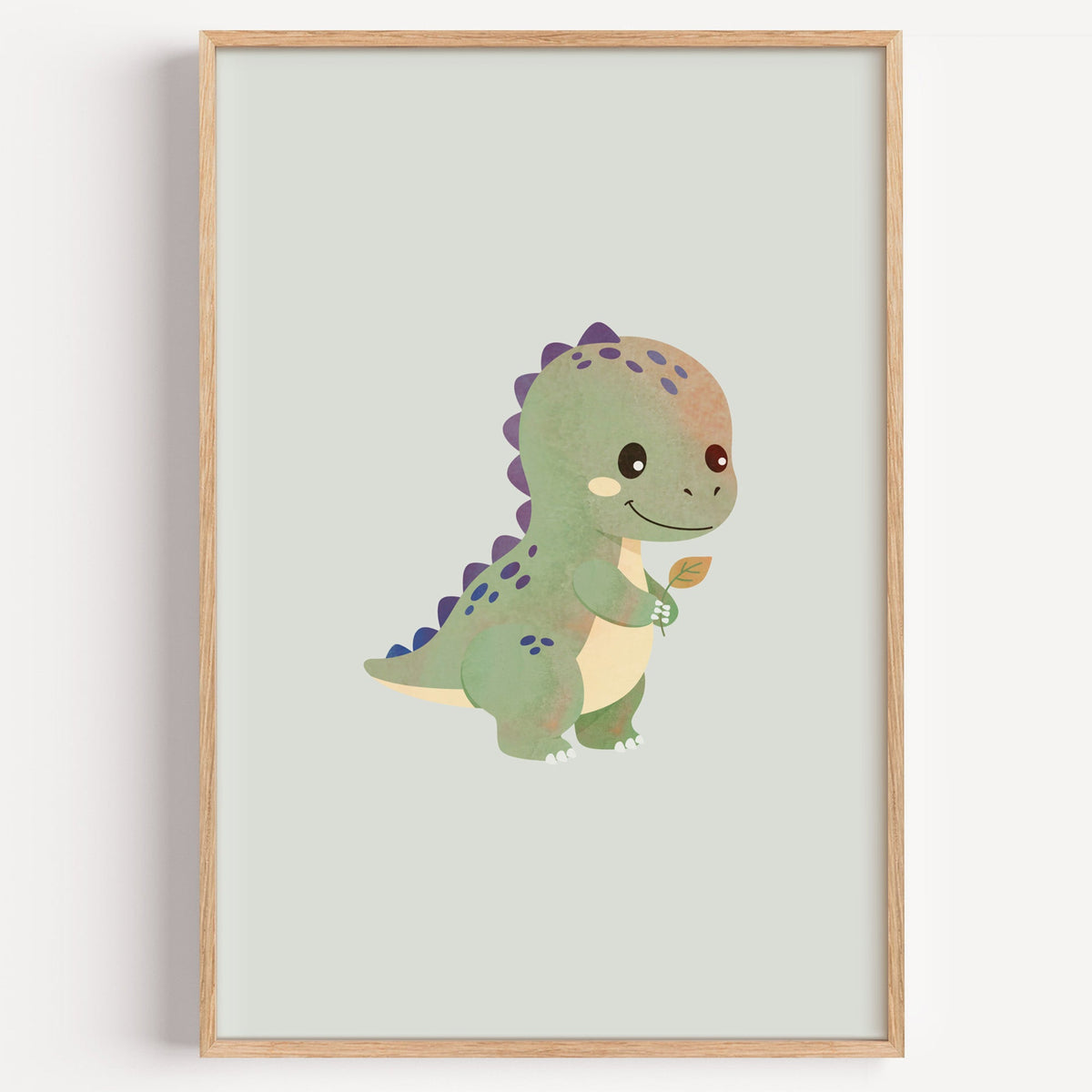 Smiling baby dinosaur holding a leaf nursery print in a light oak frame on a plain white wall