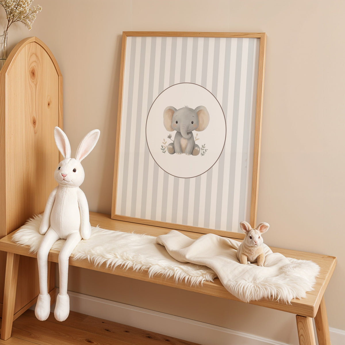 Baby elephant in a cream oval on grey stripes nursery print in an oak frame on a sheepskin bench beside a white plush bunny