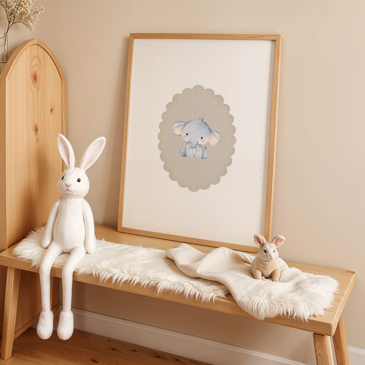 Baby elephant in beige scalloped oval nursery print in an oak frame on a sheepskin bench beside a white plush bunny