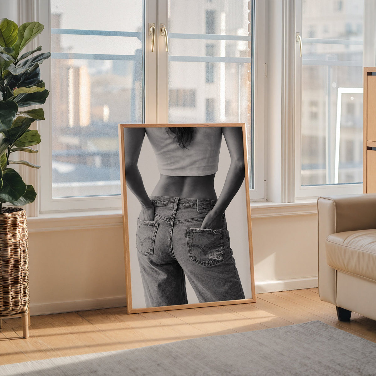 Hands in back pockets of distressed jeans print in an oak frame leaning on the floor beside a fiddle leaf fig