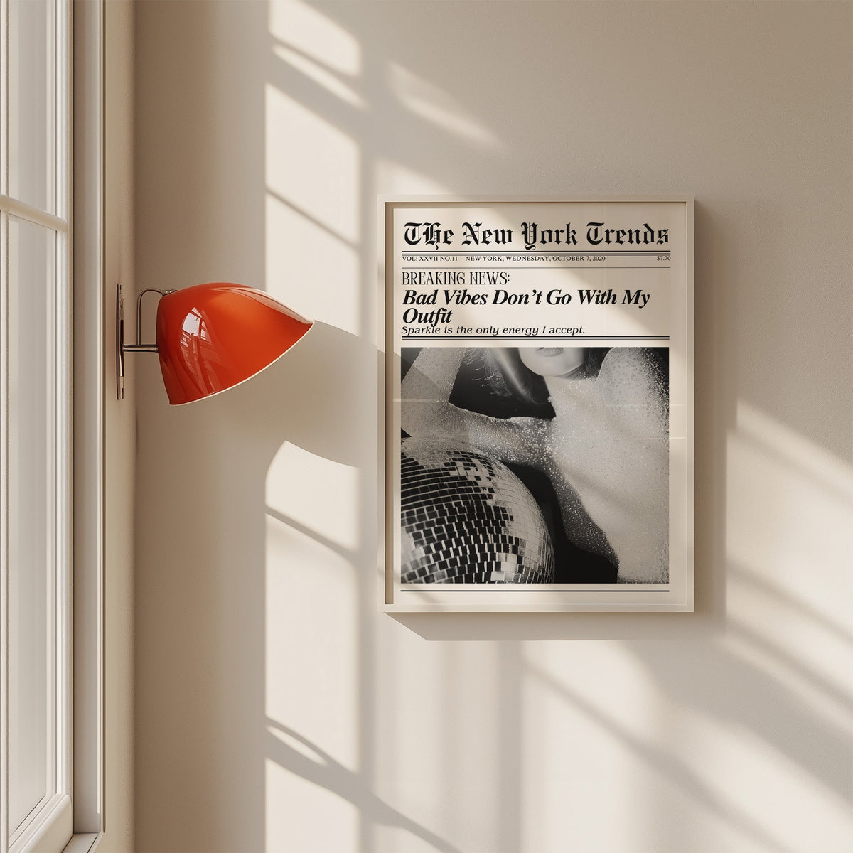 Sequin top and disco ball mock newspaper print in a white frame on a sunlit wall beside a red sconce
