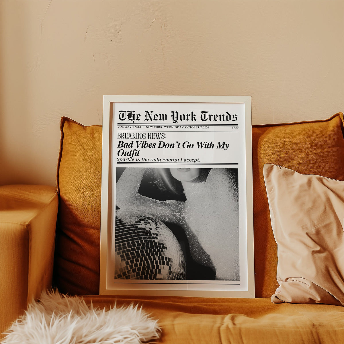 Sequin top and disco ball mock newspaper print in a white frame leaning on a mustard velvet sofa