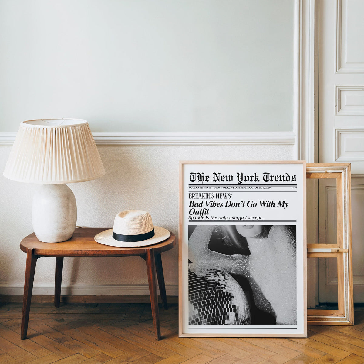 Sequin top and disco ball mock newspaper print in a pine frame on a wood floor beside a lamp and straw hat