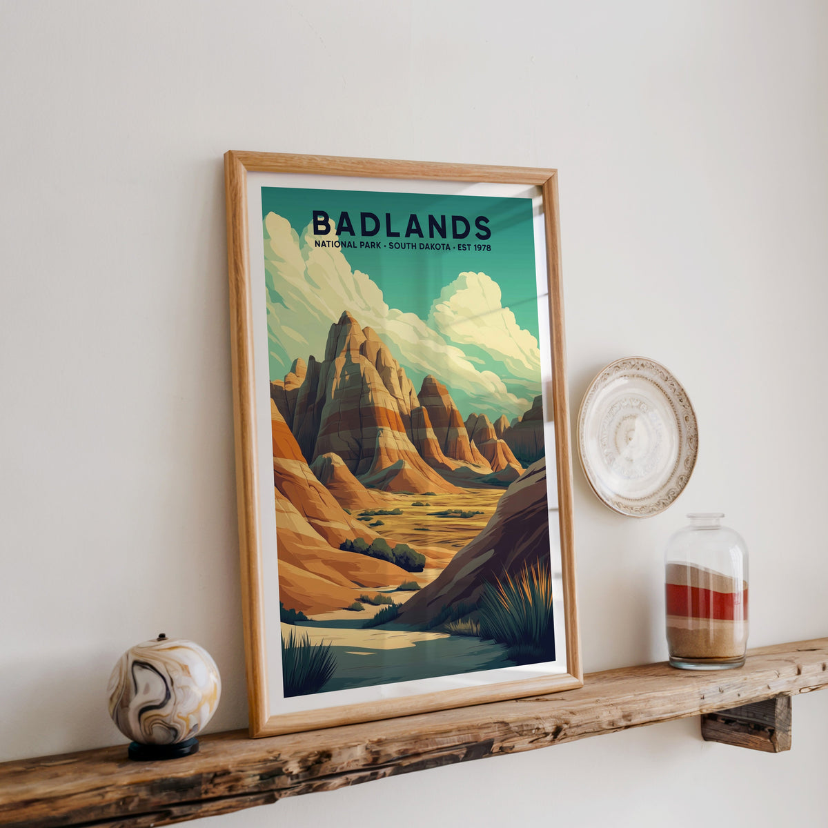 Badlands National Park print in an oak frame on a rustic wood shelf with ceramics and a sand jar