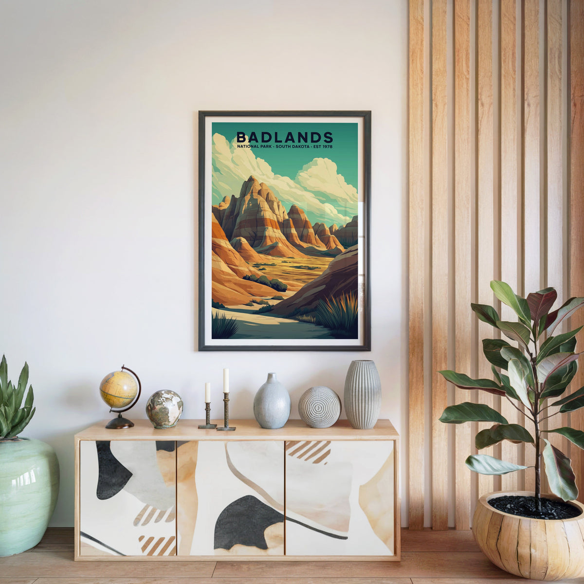 Badlands National Park print in a black frame above a light wood sideboard with a globe and vases