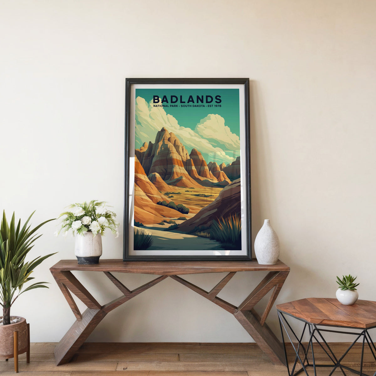 Badlands poster in a black frame on an entryway console table beside white flowers and a yucca