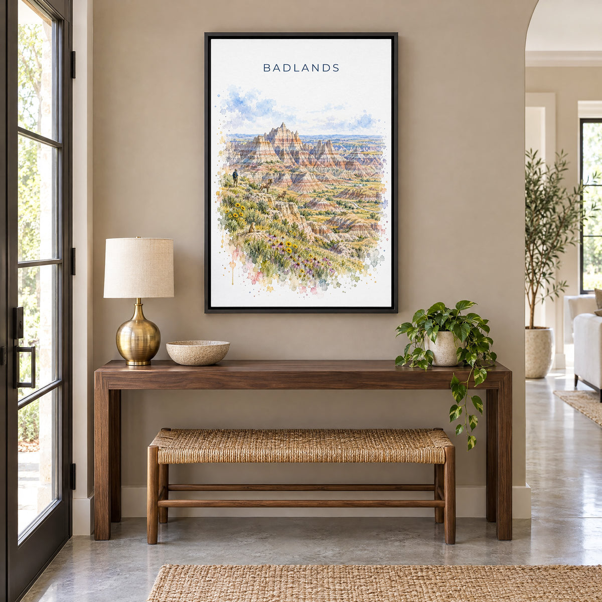 Badlands National Park watercolor print as a black floater canvas above a walnut console and woven bench in an entryway