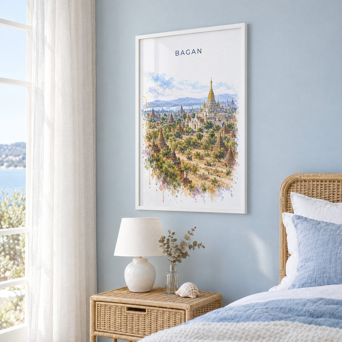 Bagan watercolor print in a white frame on a pale blue wall beside a rattan bed in a coastal bedroom