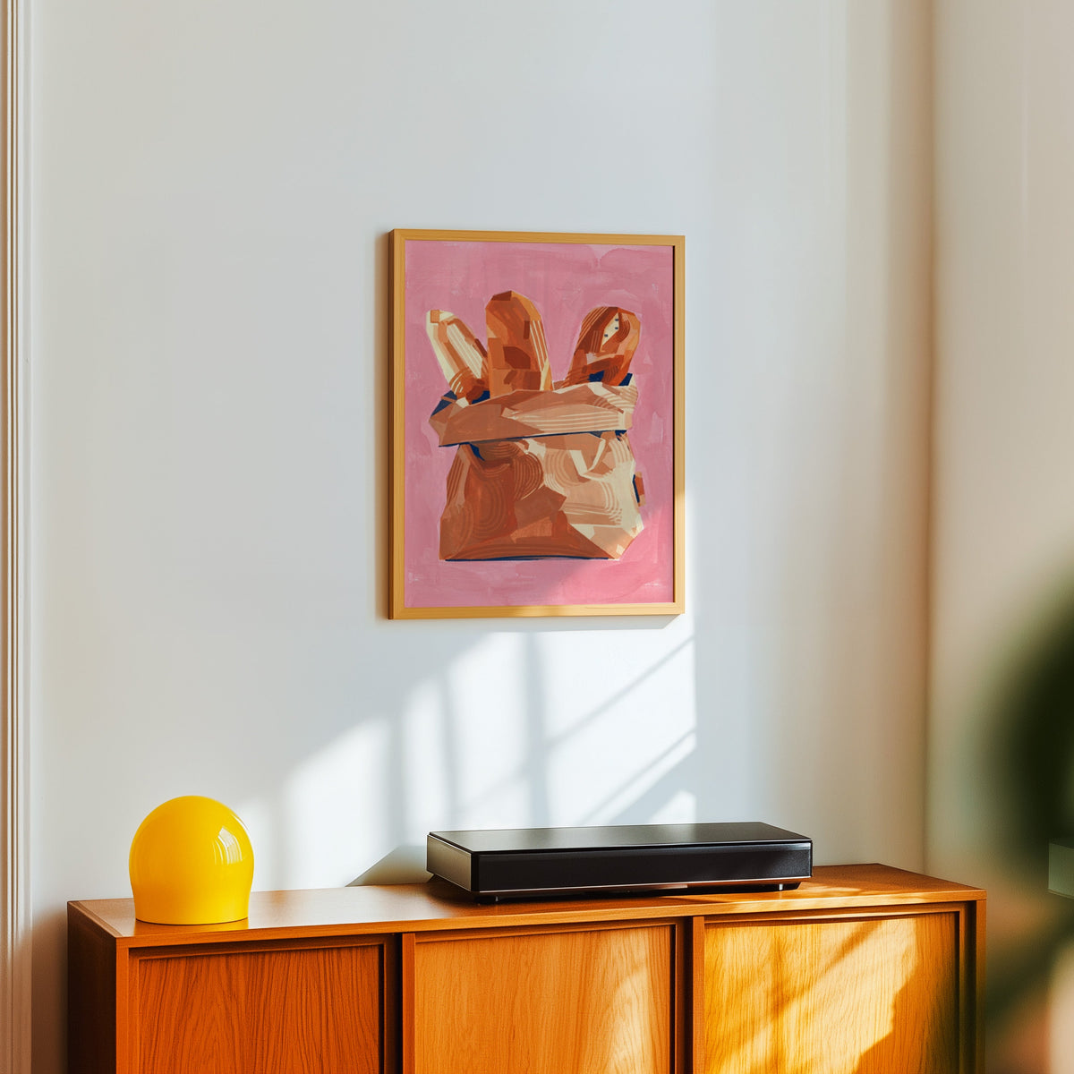 Bread bag still life print in a light oak frame above a teak sideboard with a yellow lamp