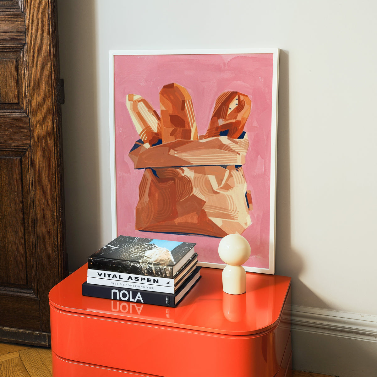 French bakery print in a white frame on a glossy orange cabinet with books