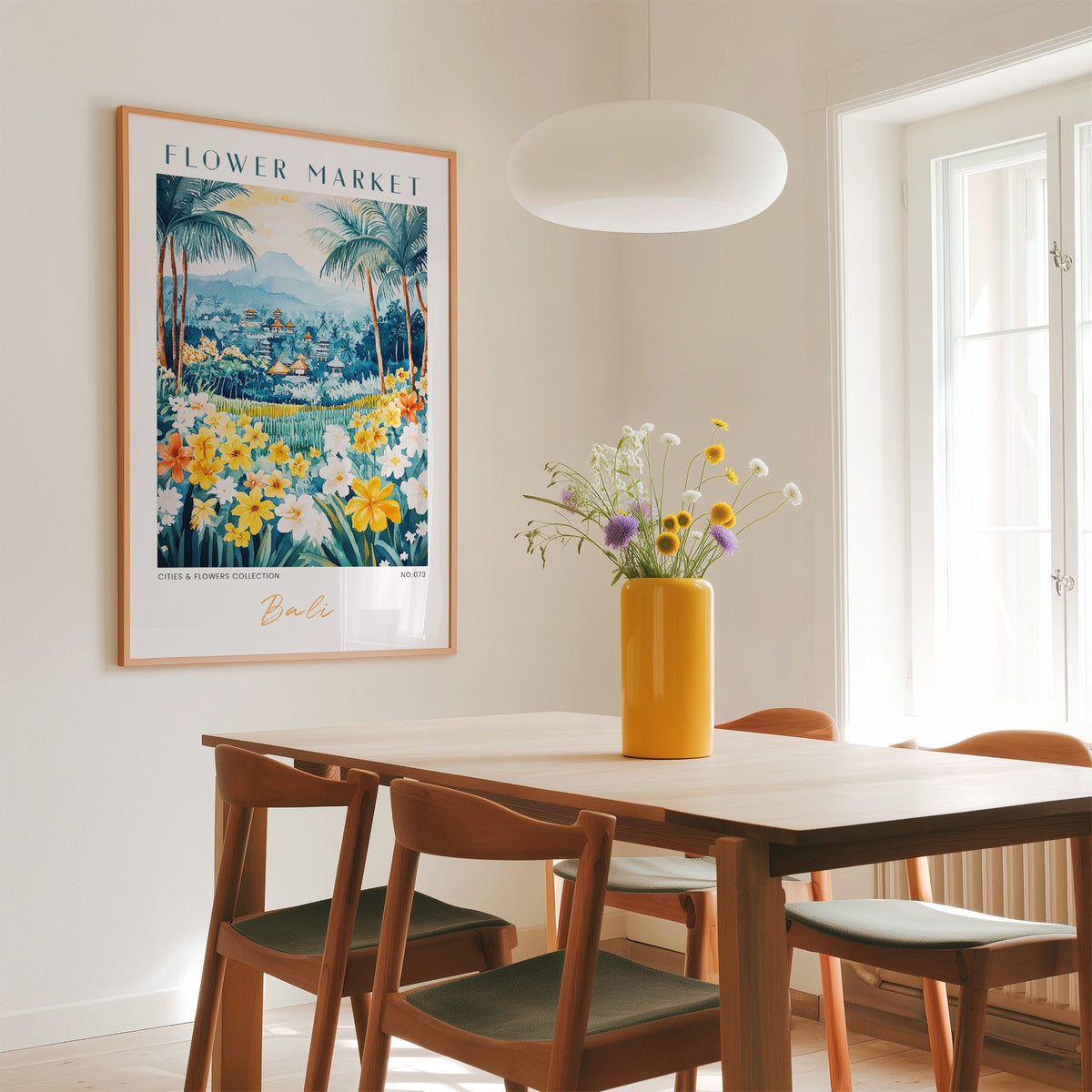 Bali flower market print in an oak frame above a dining table with a yellow vase and white pendant light