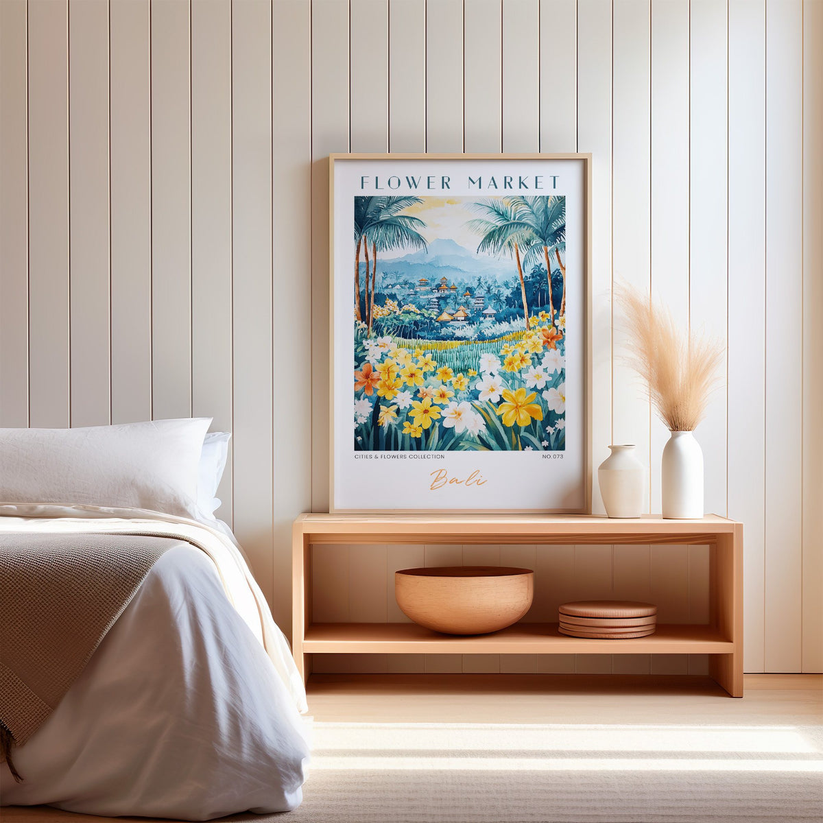 Bali flower market print in an oak frame on a wood bench against a white shiplap bedroom wall with pampas grass