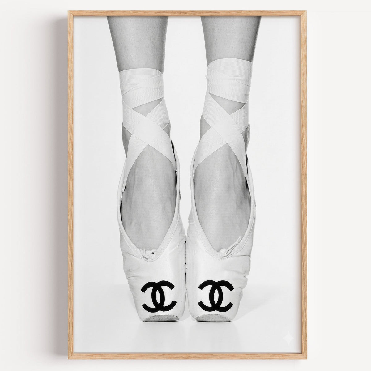 White ballet pointe shoes with crossed ribbons print in a light oak frame on a plain white wall
