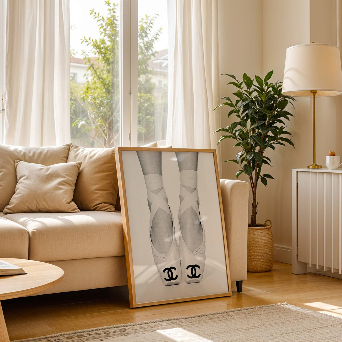 White ballet pointe shoes with crossed ribbons print in a light oak frame leaning on a cream sofa beside a floor lamp