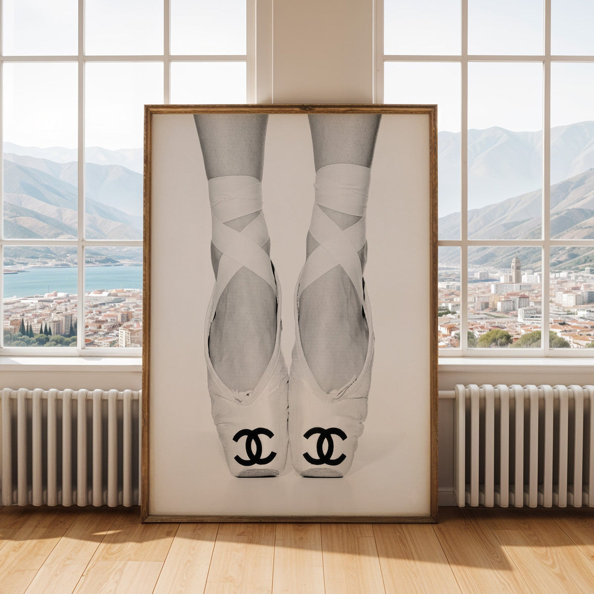 White ballet pointe shoes with crossed ribbons print shown in an antique gold frame by tall windows with a sea view