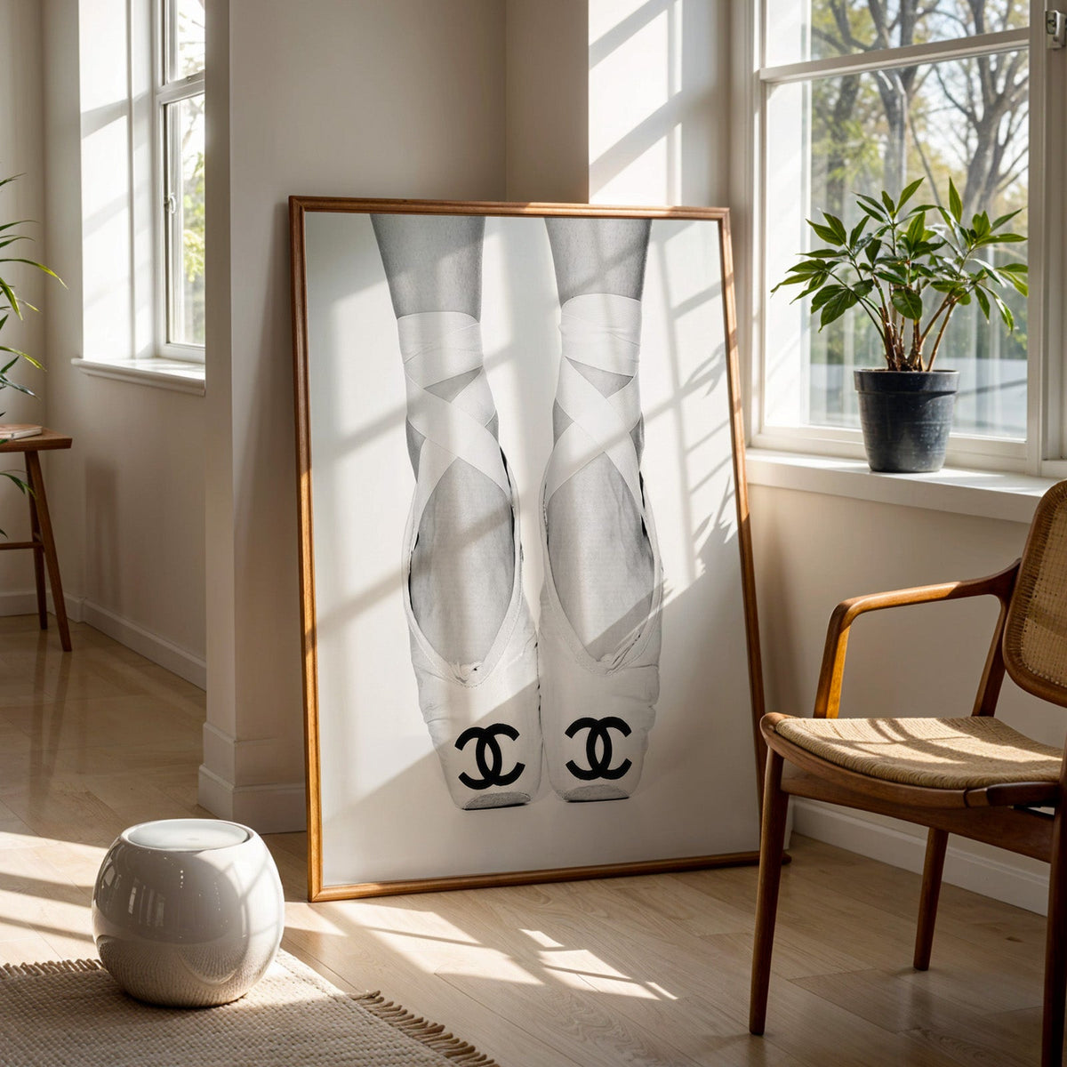 White ballet pointe shoes with crossed ribbons print in a walnut frame on a wood floor beside a cane chair and sunny window
