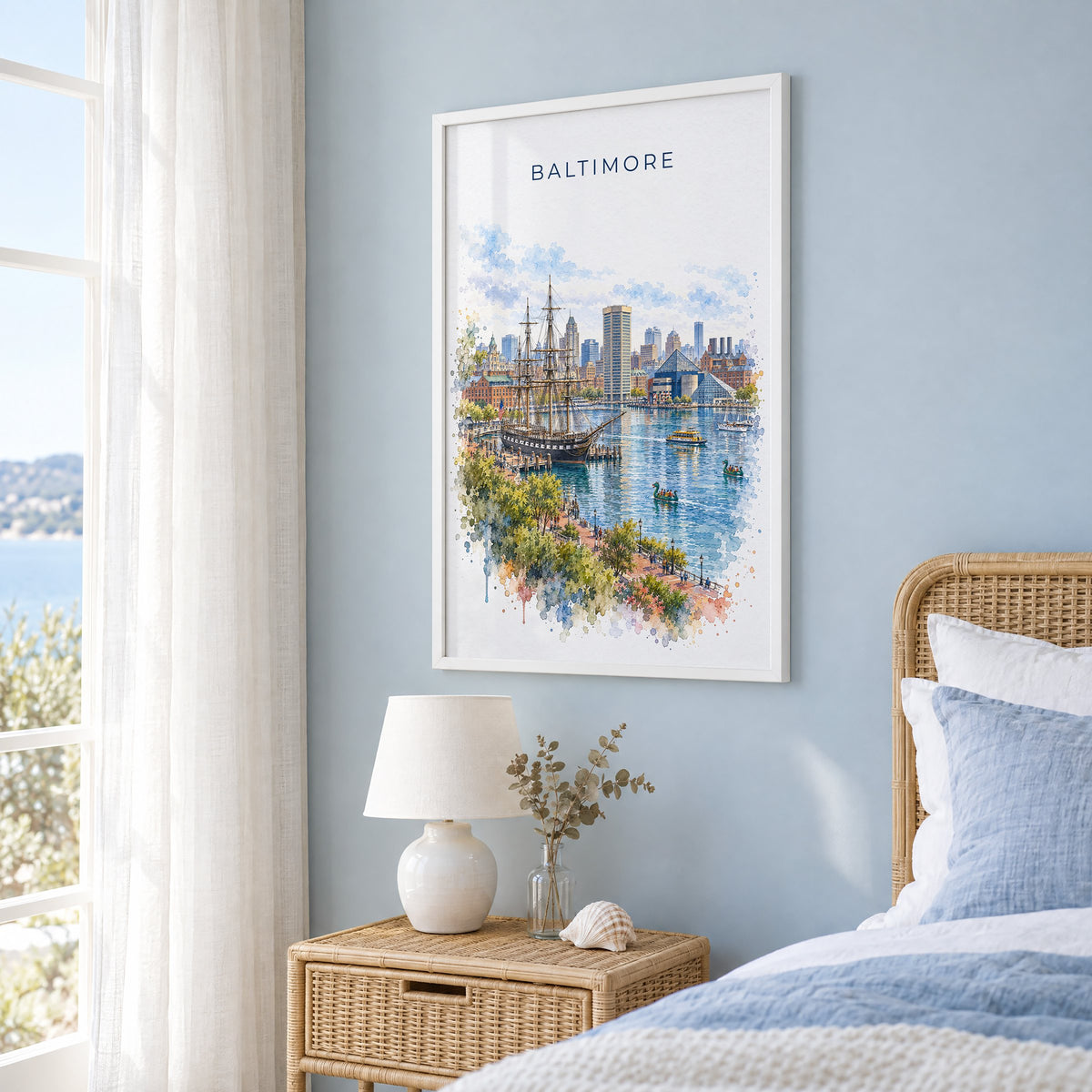 Baltimore watercolor print in a white frame on a pale blue wall beside a rattan bed in a coastal bedroom