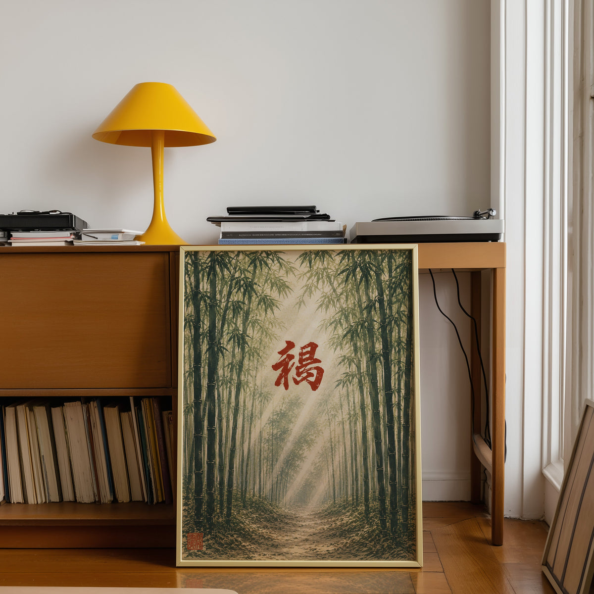 Bamboo forest red kanji poster shown in a gold frame leaning under a teak desk with a yellow lamp