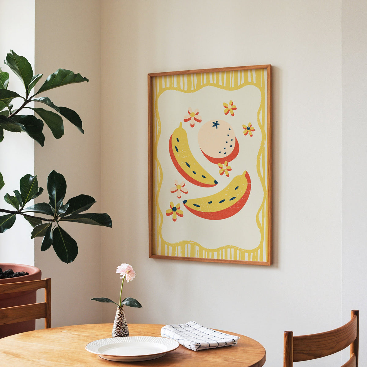 Banana and peach print in a walnut frame above a round table beside a fiddle-leaf fig
