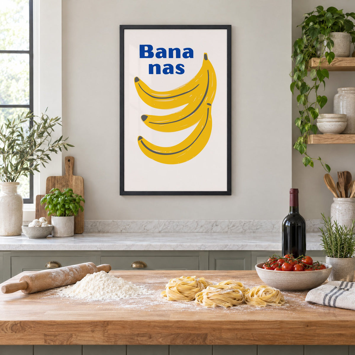 Bana nas blue type banana bunch print in a black frame above a butcher-block island with fresh pasta, flour and cherry tomatoes