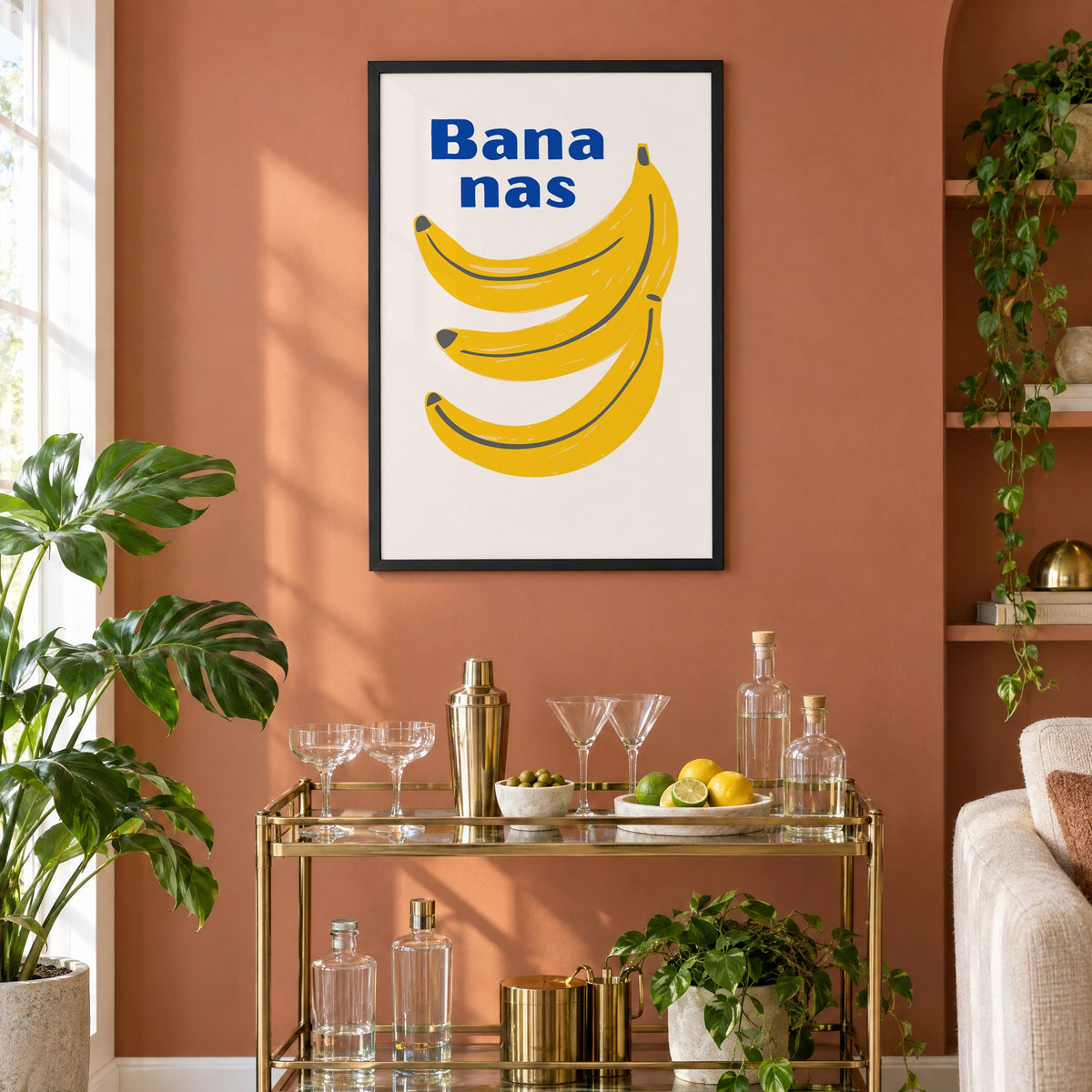 Bana nas blue type banana bunch print in a black frame on a terracotta wall above a brass bar cart with coupes and citrus