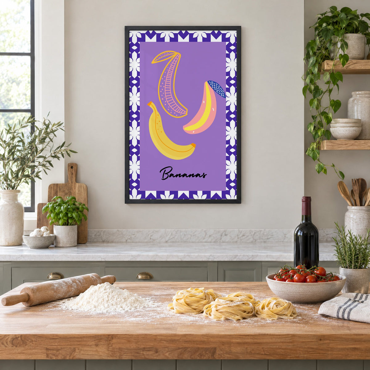Bananas doodle lavender tile border print in a black frame above a butcher-block island with fresh pasta, flour and cherry tomatoes
