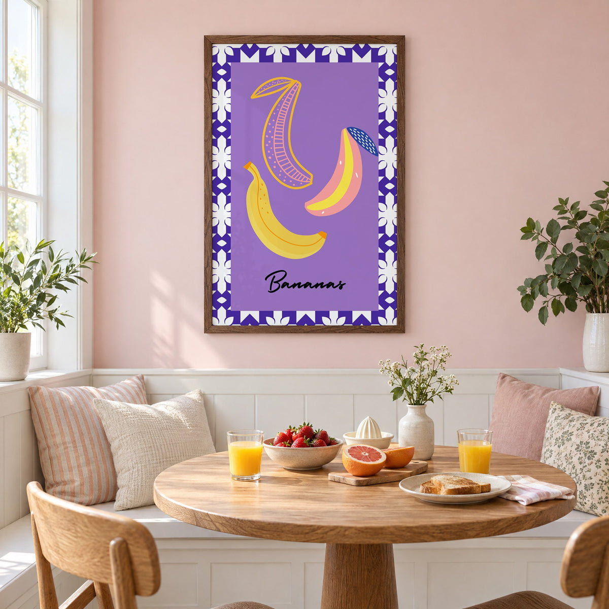 Bananas doodle lavender tile border print in a walnut frame on a pastel pink wall above a breakfast nook with strawberries and orange juice