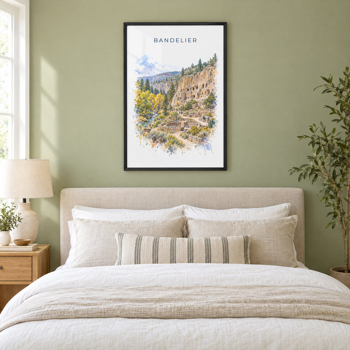 Bandelier National Monument watercolor print in a black frame above an upholstered headboard in a sage green bedroom