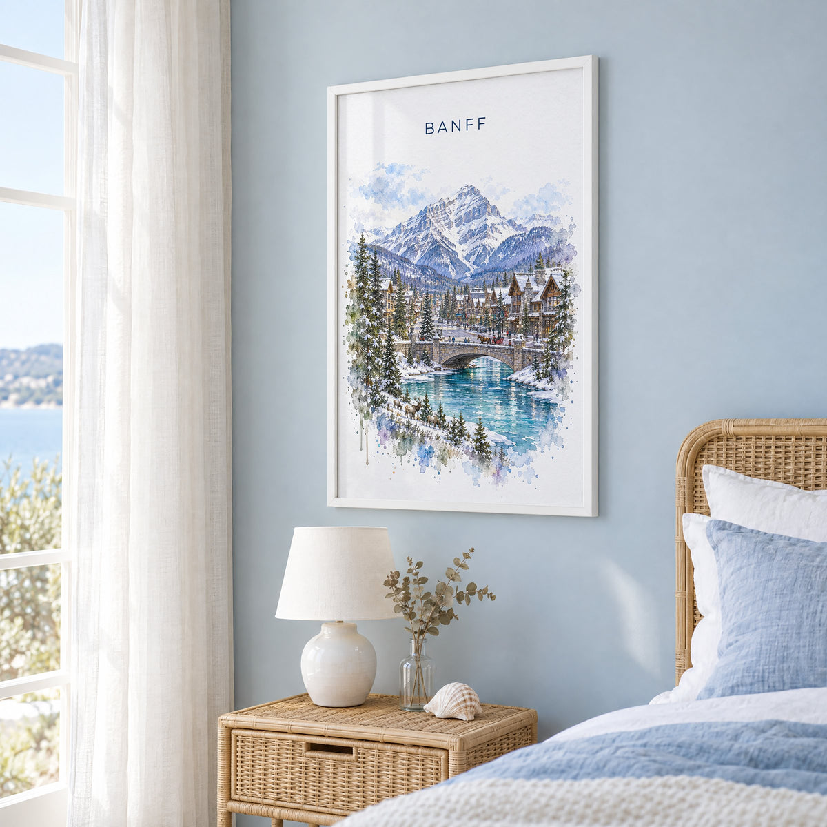 Banff watercolor print in a white frame on a pale blue wall beside a rattan bed in a coastal bedroom