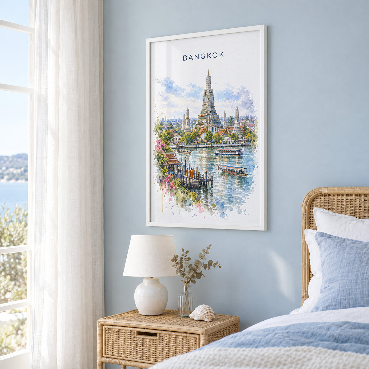 Bangkok watercolor print in a white frame on a pale blue wall beside a rattan bed in a coastal bedroom