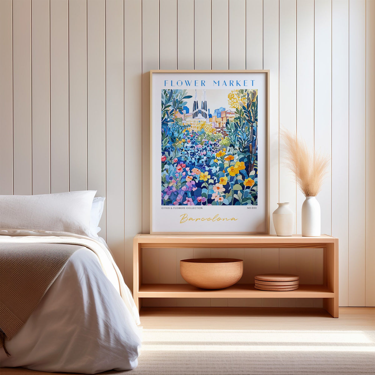 Barcelona flower market print in an oak frame on a wood bench against a white shiplap bedroom wall with pampas grass