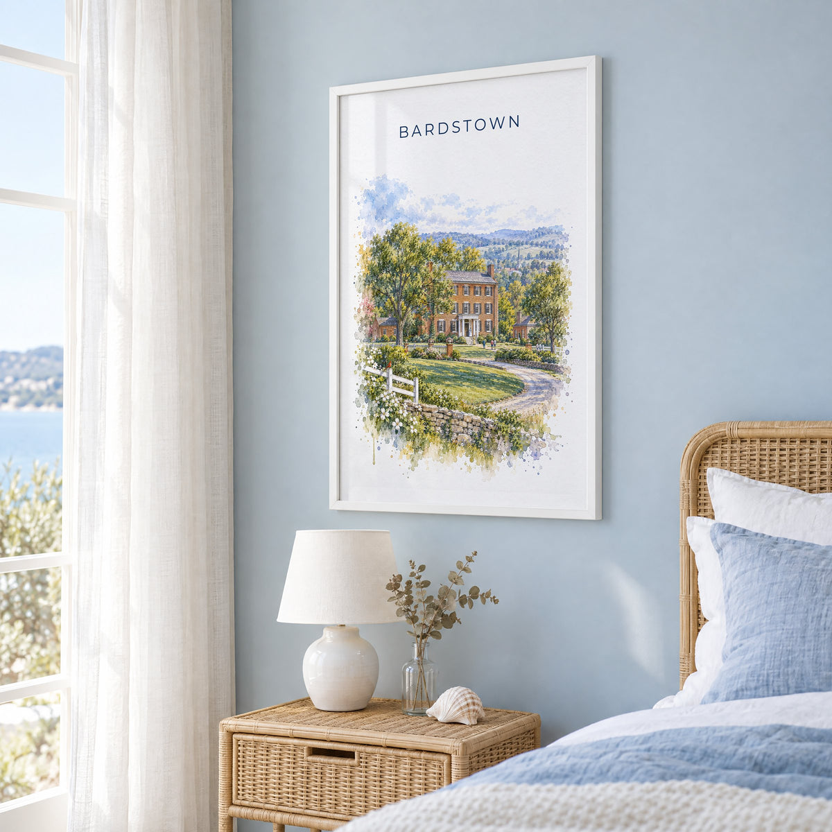 Bardstown, Kentucky watercolor print in a white frame on a pale blue wall beside a rattan bed in a coastal bedroom
