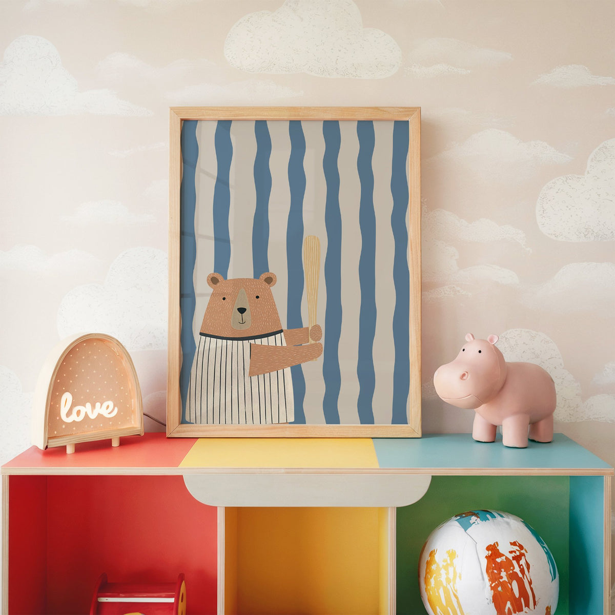 Baseball bear blue stripe nursery print in an oak frame on a rainbow toy shelf against cloud wallpaper